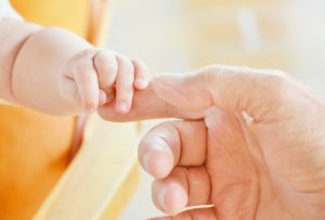 a baby's hand grasps an adult's finger on a bright yellow background