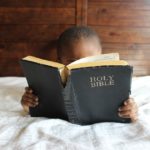 is the bible reliable A person laying in bed holds an old tattered bible up and appears to be reading from it