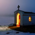 a small building with a cross on top and curved opening sits on a showy background and is lit up from the inside Is there a problem with the church