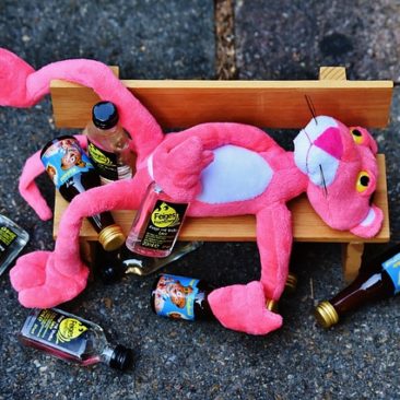 alcoholism pink panther lies on a bench surrounded by empty liquor bottles